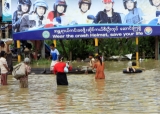 Flood victims cross the advertise helmets of poster in Bago Division, Burma.