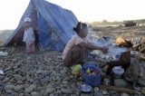 A woman of Burma's Kachin national race prepares their meal near a make-shift tent as other family members pan for gold in a river in Myitkyina, Kachin State, about 1,600 km (1,000 miles) north of Rangoon, Burma.